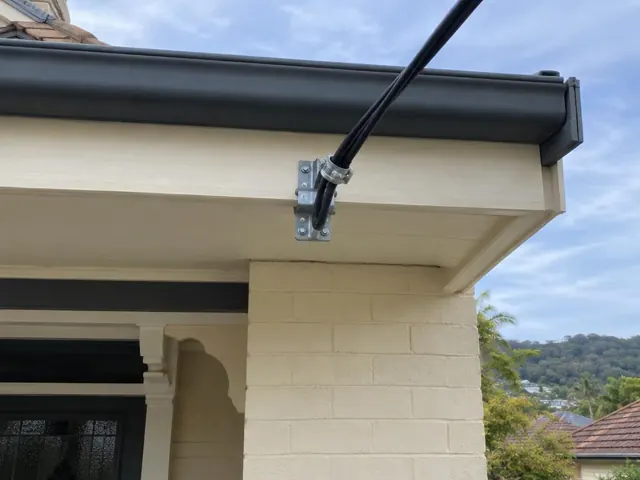 Overhead service cable and attachment bracket on a cream brick house exterior in Gosford