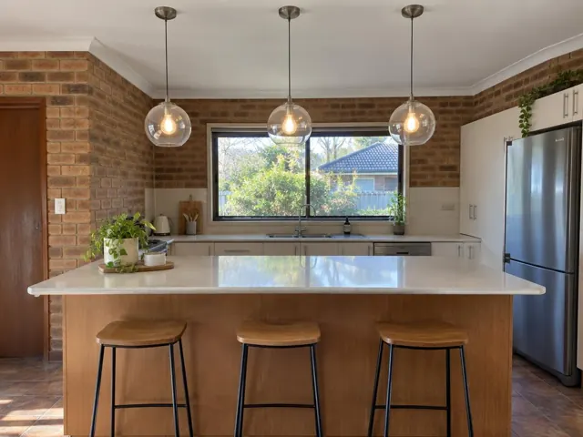 Three glass pendant lights above a kitchen island in a brick home interior in Erina